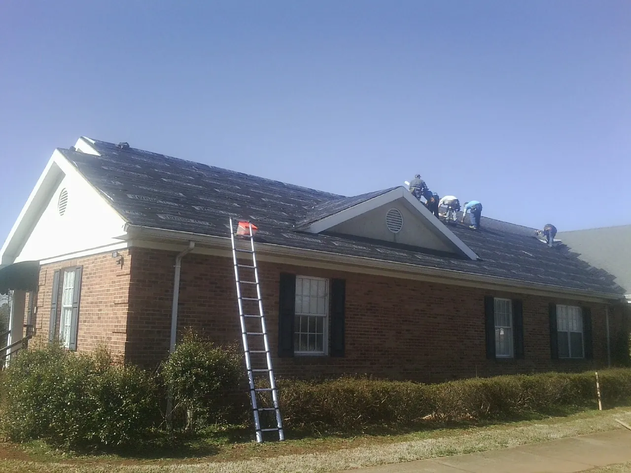 Crew tearing shingles off a brick ranch roof with a ladder set — Emergency Roof Repair work by our crew in Mokena