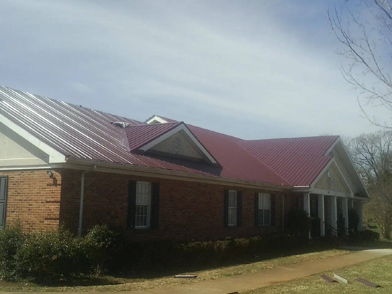 Red metal roof with gabled entries on a long brick building, from a Hail Damage Roof Repair job in Mokena