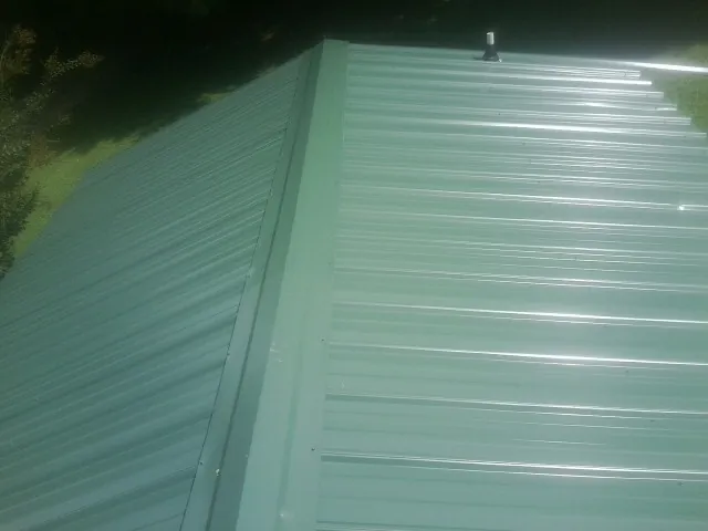 New green metal panels meeting at the ridge of a roof — Flat Roof Repair work by our crew in Mokena
