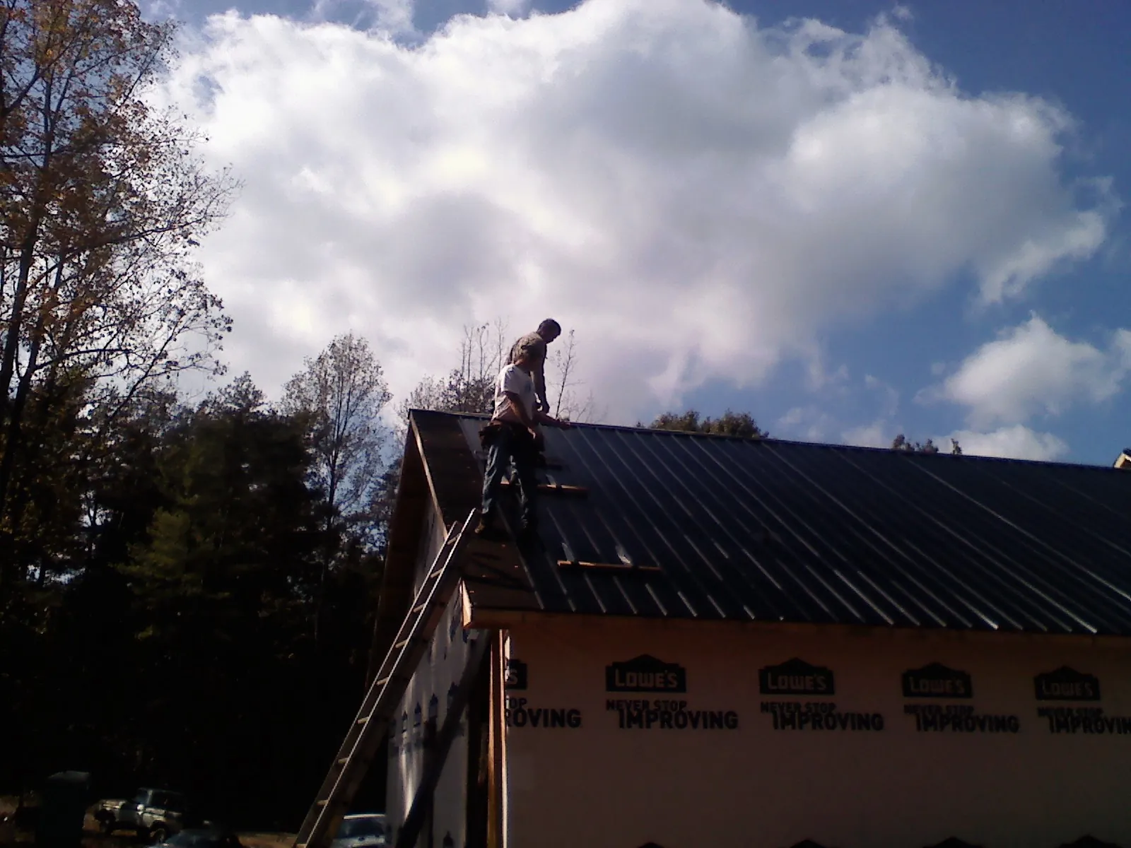 Roofer fastening dark metal panels high against a cloudy sky, from a Roof Inspection job in Mokena