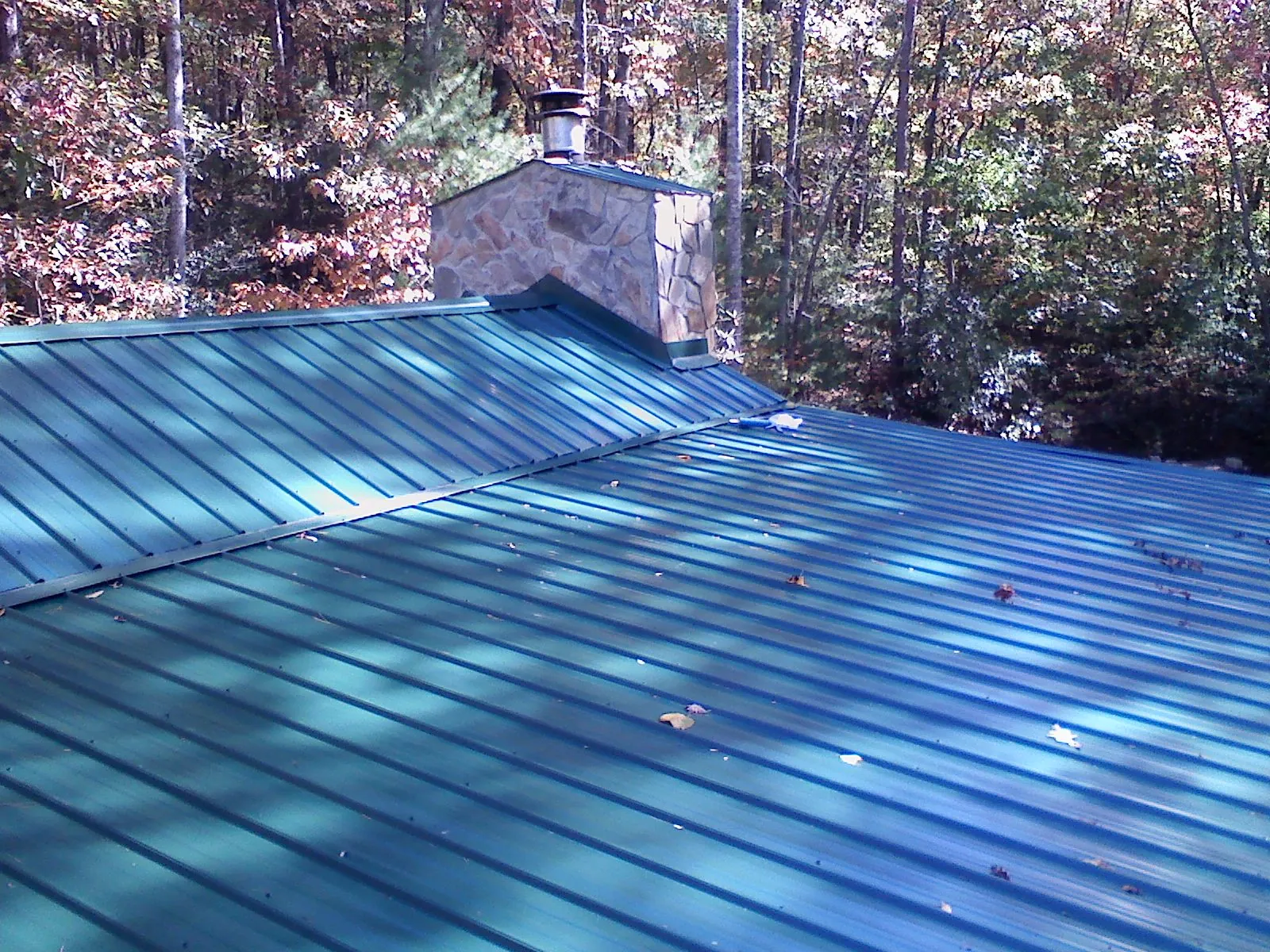New green metal roof and stone chimney surrounded by autumn woods in Mokena